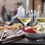 closeup of two cold glasses of white wine next to an outdoor food buffet during a party